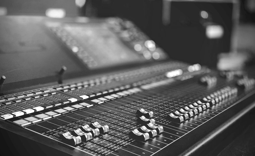 A moody black and white photo of an expensive looking mixing board.