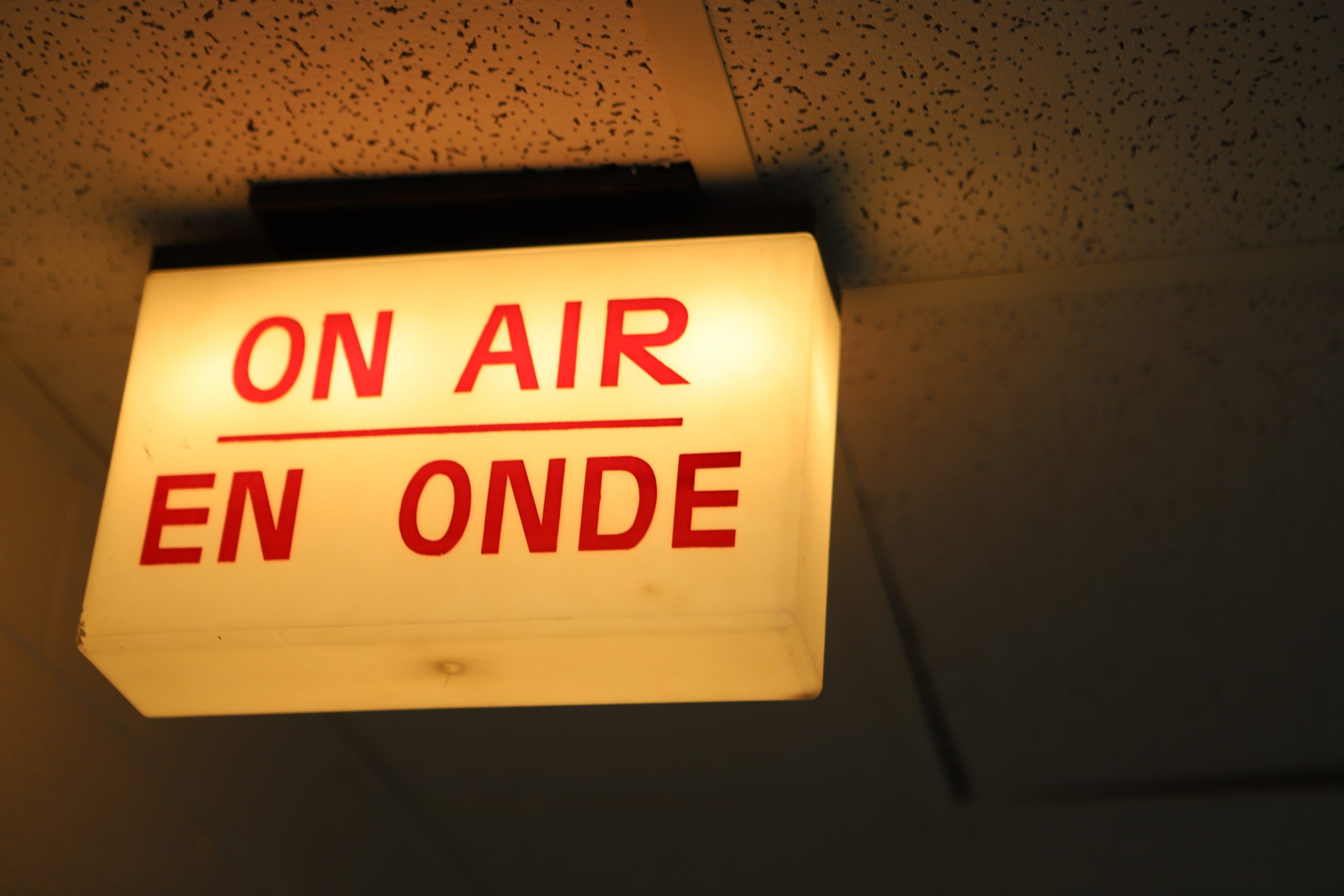 Image of an 'On Air' sign. It is lit and seen from a ceiling